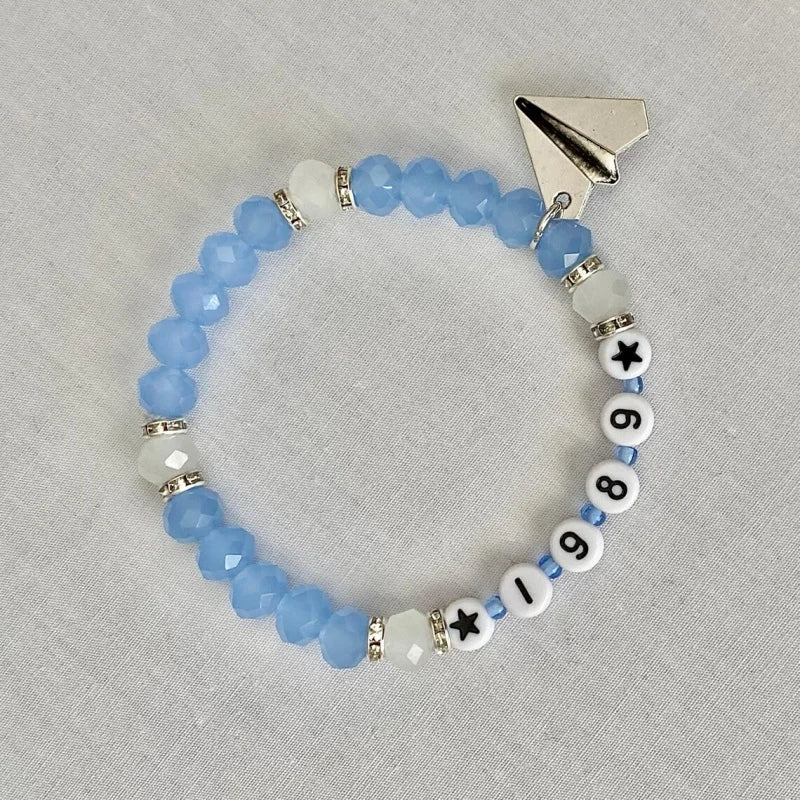 Discover the 1989 Friendship Bracelet, a Taylor Swift-inspired accessory featuring a paper airplane charm, reminiscent of the 'Out of the Woods' era. It's a perfect piece of Swiftie memorabilia for any Taylor Swift enthusiast